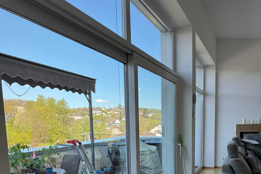 Große Fenster mit Blick auf eine grüne Landschaft und einen blauen Himmel in einem modernen Raum.